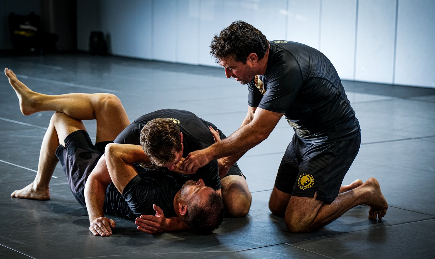 A coach instructing two athletes during a grappling session